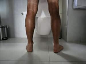 A man standing in front of a toilet in a bathroom, appearing to be using the facilities