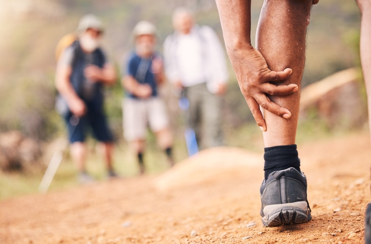 Injury, leg pain and hands of senior black man after hiking or sports accident outdoors. Training hike, elderly and male with fibromyalgia, inflammation or arthritis, broken bones or painful muscles.